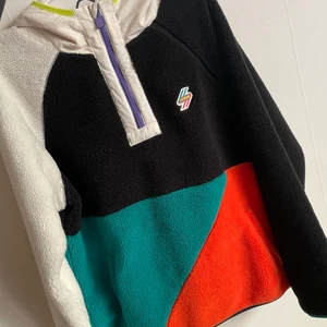 Superdry pullover - Superdry pullover vår/höstjacka i teddy/fleece i färgerna turkos, orange, svart och vit med luva. Säljer den då jag aldrig använder den, inköpt förra året för 1500kr