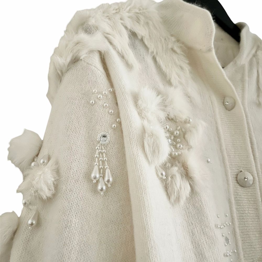 Absolutely stunning rare find that keeps your soft cozy warm and chic, this vintage 80s wool and angora cardigan is an absolute dream. It’s decorated with multiple faux pearls, rhinestones, and fox fur pompoms, worn buttoned front closure and balloon sleeves. Excellent vintage condition. One size, oversize fit.  Measurements  Length 74cm  Shoulders 53cm Sleeves 55,5cm Chest 61cm. Tröjor & Koftor.