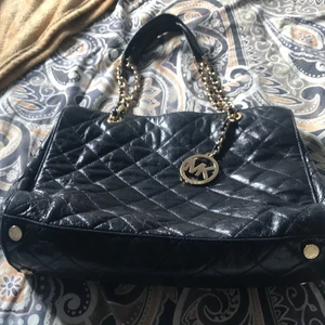 Svart Michael Kors väska - Handväska från Michael Kors, nypris 3400 kr men säljer den för 400kr då den är ganska använd. Den har 6 fickor totalt varav 2 stora med dragkedja. Rutigt mönster. Pris kan diskuteras:)