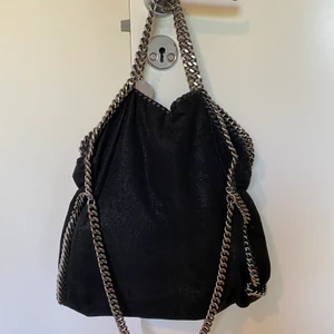 Stella McCartney Falabella Väska - Stella McCartney Falabella väska i svart. Kommer med original dust bag. Har två korta kedjor och en längre kedja för att bära crossbody eller över axeln. Seriösa bud kan diskuteras.