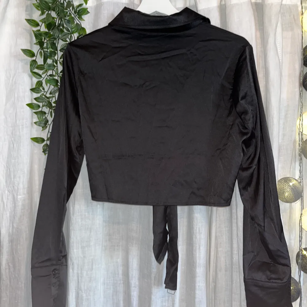 Croppad svart satinskjorta med knappar och knytdetalj framtill. Långa ärmar. Helt i nyskick. Passar både XS och S.. Skjortor.