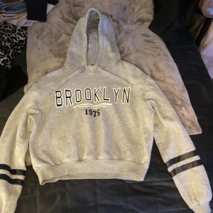 Grå cropped hoodie  - Säljer en grå cropped hoodie som det står BROOKLYN 1975 på. Från hm