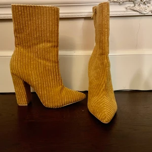 Boots m. klack - Sparsamt använda boots från Nelly med 10,5 cm klack i gult manchestertyg. Strl 36