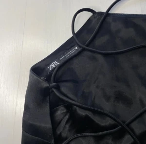 Satintopp med knytning i ryggen - Skitsnygg svart topp i satin med knytning i ryggen. Perfekt till fest eller tex nyår! Använd men i fint skick☺️