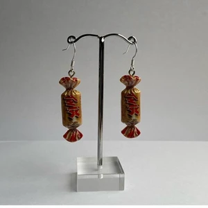 Örhängen - Detta är ett par nickelfria twix örhängen! Aldrig använda! Frakten är inte inräknad i priset utan det är 35kr + 15kr frakt! Måttet är själva twix berlocken!