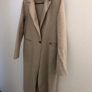Zara ullkappa strl S - Beige kappa från Zara i storlek S. Perfekt vardagskappa som passar till allt, smickrande modell fast den inte är figursydd! Är i ull/ullblandning och i väldigt fint skick. Ev. Frakt tillkommer