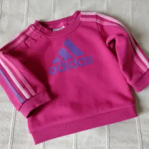 Cerise/rosa tröja/sweatshirt från Adidas. Storlek 68, UK 3-6 mån. Använd bara någon enstaka gång och i så gott som nyskick. 70% bomull och 30% polyester.