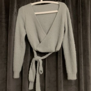 Stickad tröja - En fin stickad tröja, den är lite blåaktig och är väldigt varm! Materialet är skönt och man kan knyta en rosett på båda baksidan och framsidan! Säljer den då den inte kommit till användning!