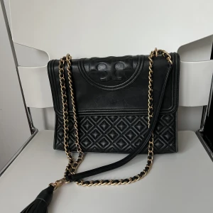 Tory burch väska  - Säljer min fina tory burch väska i modellen ”Fleming”. Den stora modellen. I bra skick men finns slitningar på ovansidan av väskan (kan skicka bild om så önskas).