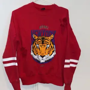Sliten sweatshirt med motiv av en tiger. Köpt på Gina Tricot för 299kr. Använd några gånger. Tröjan ska vara sliten, så oroa er inte haha. Röd färg med vita stripes på ärmarna. Storlek XS men oversized.