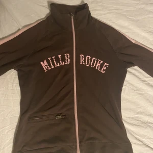 brun zip up  - Brun zip up med rosa sträck på ärmarna, och rosa bokstäver där fram.