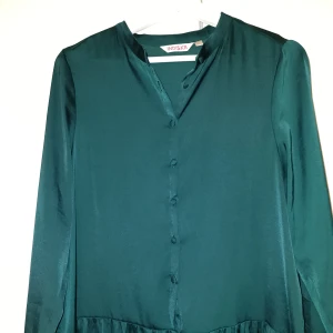 Mörkgrön klänning Indiska  - Mellanlång klänning med knappar. Mörkgrön och blank i tyget. Fint material och i nyskick.