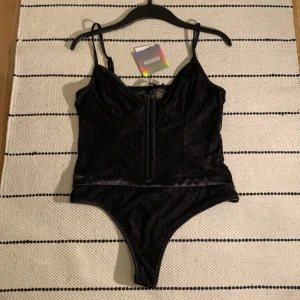 Svart Spetsbody  - Svart spetsbody från Missguided, storlek eu 38. Korsettliknande men inte lika ”fast” och bygellös. Baksidan av bodyn är i spets och genomskinlig. Ej använd, prislapp fortfarande kvar!