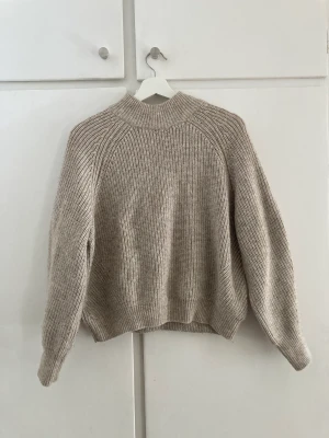 Beige/rosa stickad tröja - Beige stickad tröja med rosa underton. Rundad och ganska kort nertill vilket gör att den sitter snyggt och inte blir ”säckig”. Ser grå ut på bilderna men är mer beige/rosa. Säljes då den är för liten.
