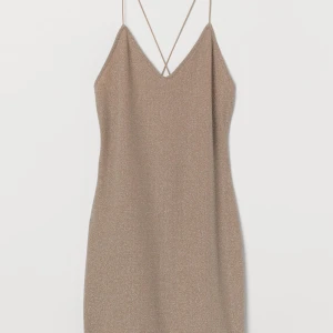 Glittrig tajt klänning  - Beige / Nude kort mini klänning i glittrig trikå. Djupt v-ringad och smala elastiska axelband som är korslagda i ryggen. Storlek XXS  Aldrig använd, nyskick