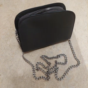 Väska - Jätte snygg svart väska med kedja, från H&M. Den är i bra skick. Säljer då den inte kommer till andvändning längre.  80kr+frakt