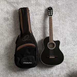 Ortega PRO Gitarr RCE141BK + deluxe gig bag. Nypris 4790:- - Ortega's RCE141BK is an electro-acoustic classical guitar from the Family Pro series. It has a mahogany back and sides with a solid spruce top and a black high gloss finish. The white and abalone binding adds a nice colour contrast which takes its appeara