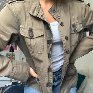 Militärgrön vårjacka - Jättenice vårjacka med detaljer på axlarna. Passformen är ganska lös så man kan absolut ha en tjocktröja under eller inte.