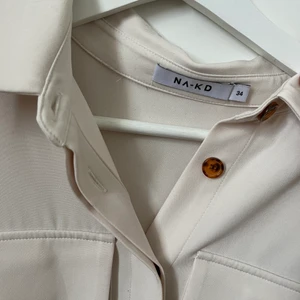 Klänning från NA-KD - Klänning med knappar och knyte i midjan, från NA-KD. Använd 2 gånger, fint skick. Krämvit/beige i färgen 