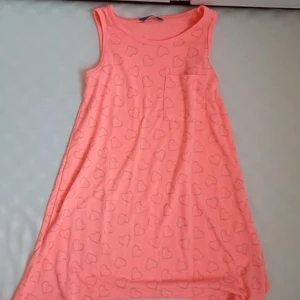 Korall färgat linne/klänning för mindre barn st 122 - Ett korall färgat linne/klänning (osäker på vad det är) i st 122, alltså för lite mindre barn. Den har silver hjärts mönster och en liten bröst ficka.