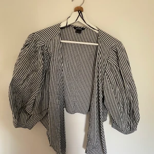 Blus skjorta - Svart/vit rutig blus/skjorta som knyts fram. Den har stor puffärm/ballongärm. Sval och skön! Använd fåtal ggr, väldigt fint skick!