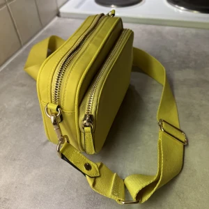 Oanvänd väska  - Oanvänd väska som höjer och sätter färg på din outfit. Två yttre fack, justerbart band med guldspännen/dragkedja och mycket rymlighet. Pappen/plasten kvar i insidan så den har hållit sin form, precis som när den köptes. 