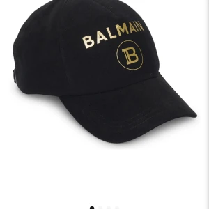Balmain keps - Balmain cotton cap svartguld.  Helt oanvänd från nk i Stockholm , nypris 2699.  Lappen finns kvar och inget kvitto tyvärr.