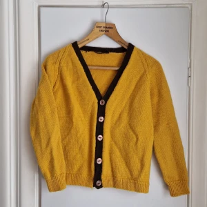 Gul retrokofta / VINTAGE  - Klargul stickad kofta med bruna kanter och bruna knappar.  Gissningsvis ull eller ullblandning. Medeltjockt och tätt stickat. Uppskattas till en stl S/36. Otroligt fin till blåjeans eller jeanskjol, med en cool retro-tisha under. Även klänning. 36/38