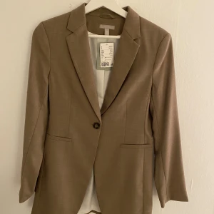 Kavaj - Beige kavaj från h&m. Helt oanvänd och ny. Köpte men den passa inte riktigt mig (lite lång i armarna på mig som är 160) men glömde att lämna tillbaka. ): så nu säljer jag den istället, nypris 499kr