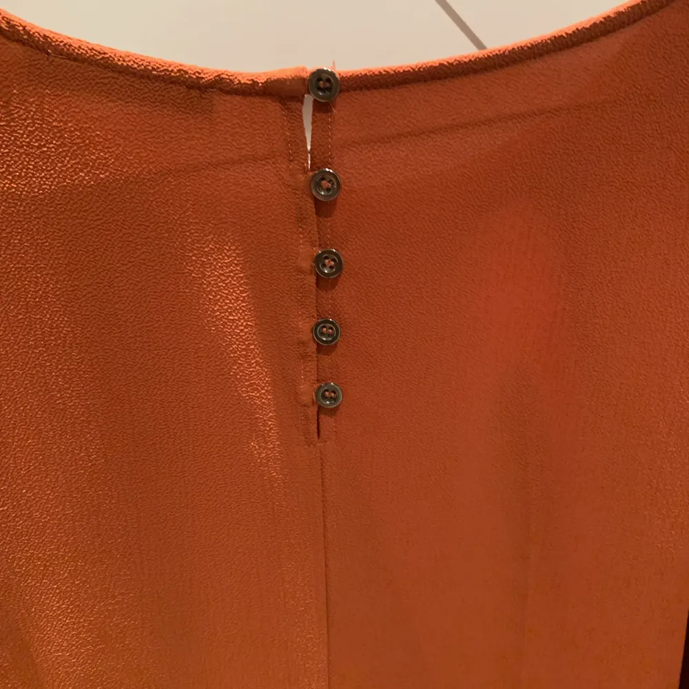 Mörkt orange blus med snygga knappdetaljer i nacke och ärmslut. Volang nedtill. Endast använd ett fåtal gånger. . Blusar.