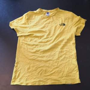 En helgul t-shirt från North Face. Svart liten logga både back och fram. Plagget är i ok skick, inget slitage. 