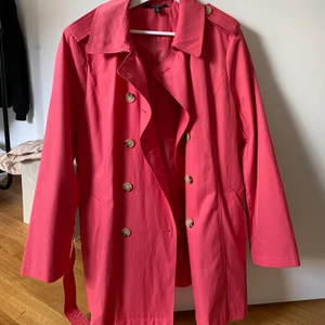 Kort rosa trenchcoat - Säljer denna riktigt coola trenchcoat från Ralph Lauren. Den kommer inte till användning tyvärr men den är riktigt snygg till sommar! Inte lika skrikig i färgen i verkligheten, typ hallonröd. Lårkort (på en runt 163cm). Aldrig använd, så den är i riktigt bra skick! Nypris 1500, säljer för 500