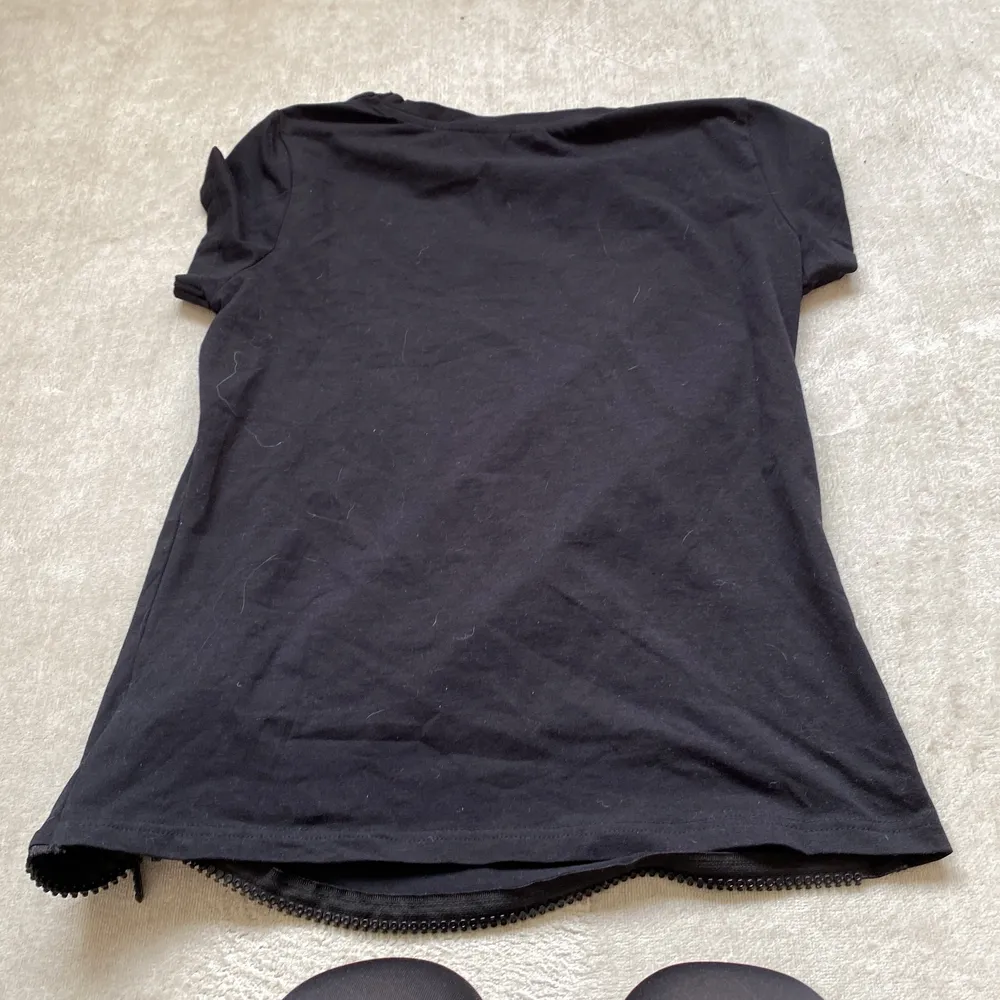 Det är en svart t-shirt som är oanvänd som har en kedja som kan röra sig . Paidat.