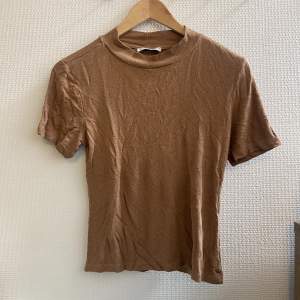 T-shirt från Gina Tricot i en mörkbeige färg. Har legat bortglömd och blivit skrynklig och har en del noppor, men det borde kunna åtgärdas. 