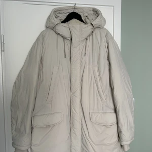 ARKET lång pufferjacka - ARKET lång pufferjacka (Herr) Storlek L Färg: off-vit Skick: som ny Material: Foder: Polyester 100%, Vaddering: Dun 80%, Fjäder 20%, Ytterlager: Återvunnen polyester 52%, Återvunnen polyamid 47%, Foder: Återvunnen polyester 100%