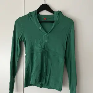Grön tröja med luva, knappar och knyt runt midjan som jag säljer för att den inte riktigt är min stil!💚 Skicket är bra inga defekter men är köpt av mig på second hand!🥰