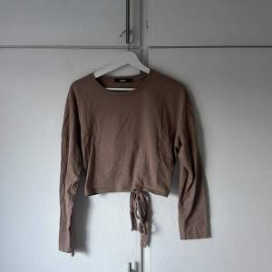 Ljusbrun/begie croppad långärmad tröja som har en öppning i ryggslutet med knyte. Köpt från bikbok och använd enstaka gånger.  Storlek M