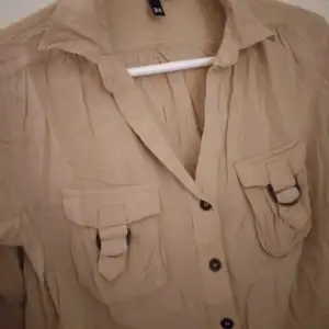 Beige snygg blus. Strk: 34. Material: Mjuk och luftig Viskos. Felfri.  Har 2 bröstfickor med spännen, resår i midjan, reglerbara ärmar. Säljer även en likadan, fast svart.