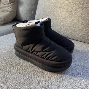 UGG maxi mini boots, vinterstövlar / snowboots i puffermaterial med varmt foder. Därav tåligare än vanligare uggs men lika varma! Köpte tyvärr en för liten storlek för mig och därför säljer jag dem. Oanvända/ nya, enbart testade.   Färg: Svart Storlek: 37