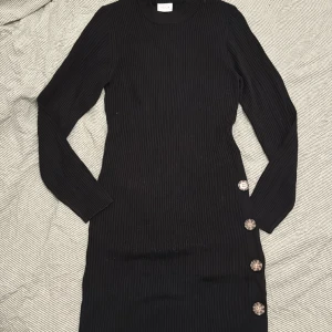 Stickad klänning  - Svart stickad klänning med knappar på sidan som detalj. Ganska tunn med ribbat tyg. Använd 1 gång.