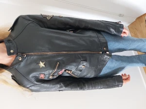 Skinnjacka med patches - Läderjacka i strl S men skulle passa XS. Har unika patches och i bikerstil. Saknar dock en knapp på vänster axel.
