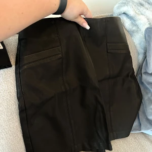 Svart skinnkjol - Säljer en svart skinnkjol (ej äkta skinn), som har silvrig dragkedja bak. Kjolen är endast använd vid ett tillfälle, så mycket fint skick. Färg: Svart Storlek: 40