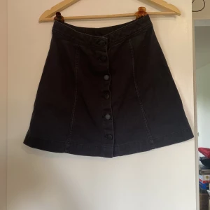 Svart jeanskjol med knappar - Sparsamt använd i fint skick.går halvvägs ner på låret på mig som är 166 cm. Hör gärna av dig vid frågor eller för fler bilder. Köpare står för frakt.