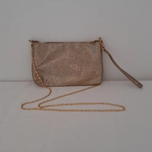 Ny Glittrig handväska - Ny oanvänd Lindex superfestlig handväska. Glittrig och härligt gnistrande. Avtagbar handrem och axelrem. Stängs med dragkedja. Gulddetaljer.