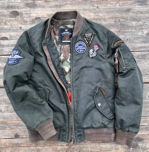 Superdry Rookie Edition Bomberjacka  - Tuff höstjacka, militärgrön. Bra skick, dock en liten skada på innerfodret, lätt att fixa. Storlek S ( 158-164 cm skulle jag tippa på )
