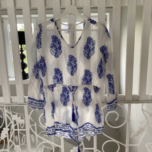 Kort tunn jumpsuit - En tunn och sval jumpsuit i vitt med blått mönster. Inget att anmärka på så i fint skick. Aningen genomskinlig.  Det står att den är i strl L men tycker den är mer som XS-S. 