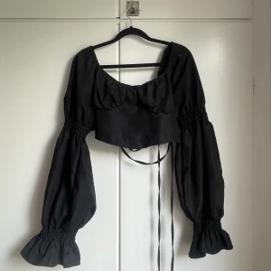 Svart topp med knytning  - Jättefin topp med knytning i ryggen. Lite puffiga ärmar som syns på sista bilden. Använd endast 1 gång