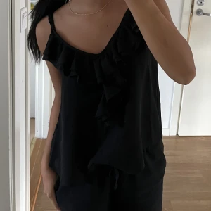 Svart linne med volang - Linne med volang, fint skick! Plagget har även justerbara axelband vilket är ett + 💓