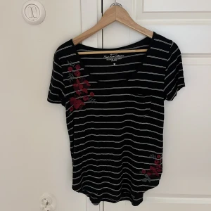 T-shirt  - Svart T-shirt med vita ränder och blombroderi på. Mjukt material.