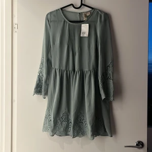 Klänning XS - Kortare klänning i ”genomskinligt” blus material. Spets på ärmar och vid klänningens slut. Sydd i midjan.   Mint grön  H&M Divided  Storlek: XS/34  Helt ny, prislappar kvar! 